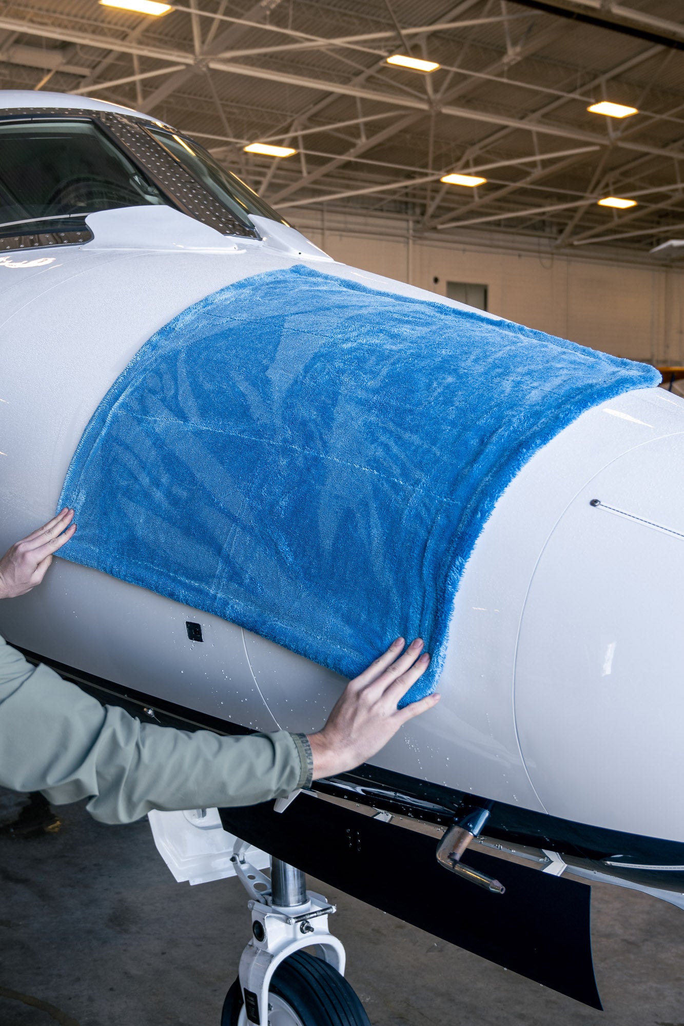 Large blue microfiber drying towel laid over white airplane nose in indoor hangar setting