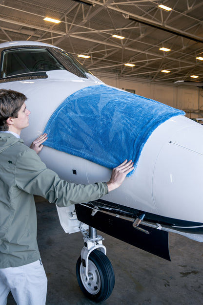 A large blue microfiber drying towel draped over the nose of a white airplane in a hangar setting