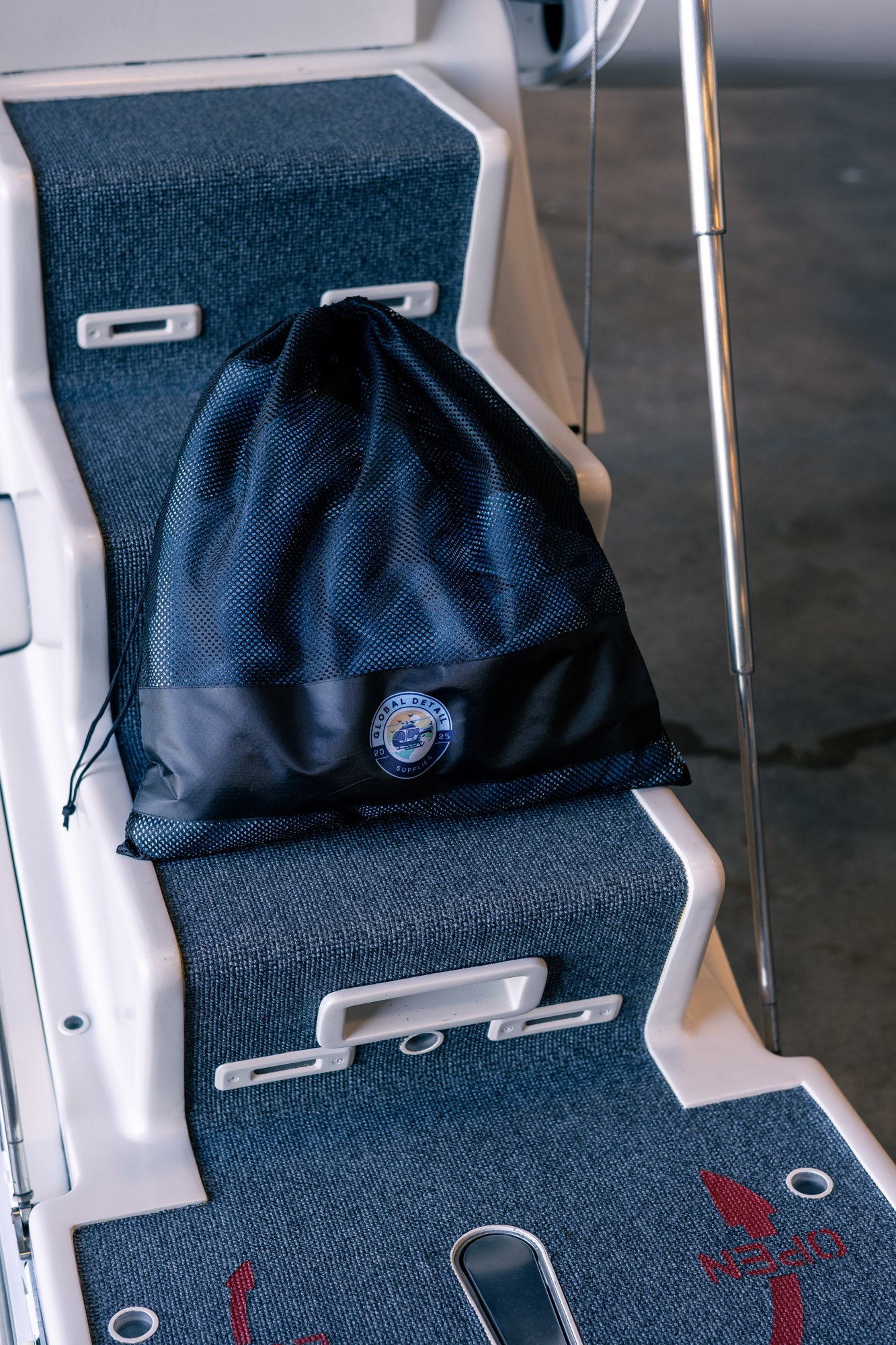 Black mesh drawstring bag with circular branded patch sitting on gray carpeted surface of boat deck steps