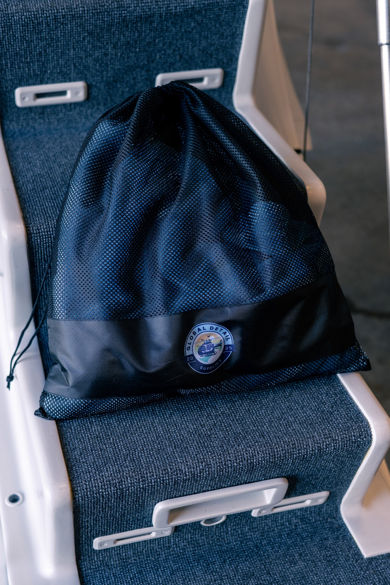 Black mesh drawstring bag with circular logo resting on blue carpeted boat seat or step