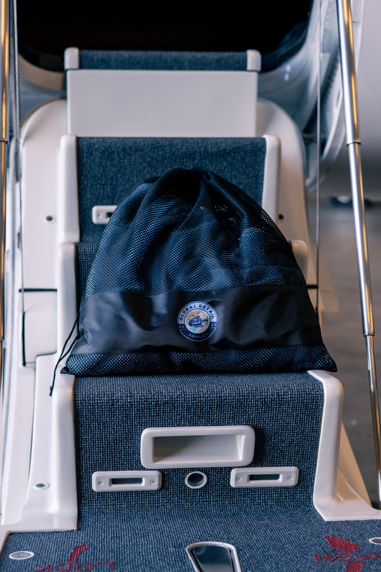 Black mesh storage bag with Global Detail logo placed on marine boat steps covered in blue carpet
