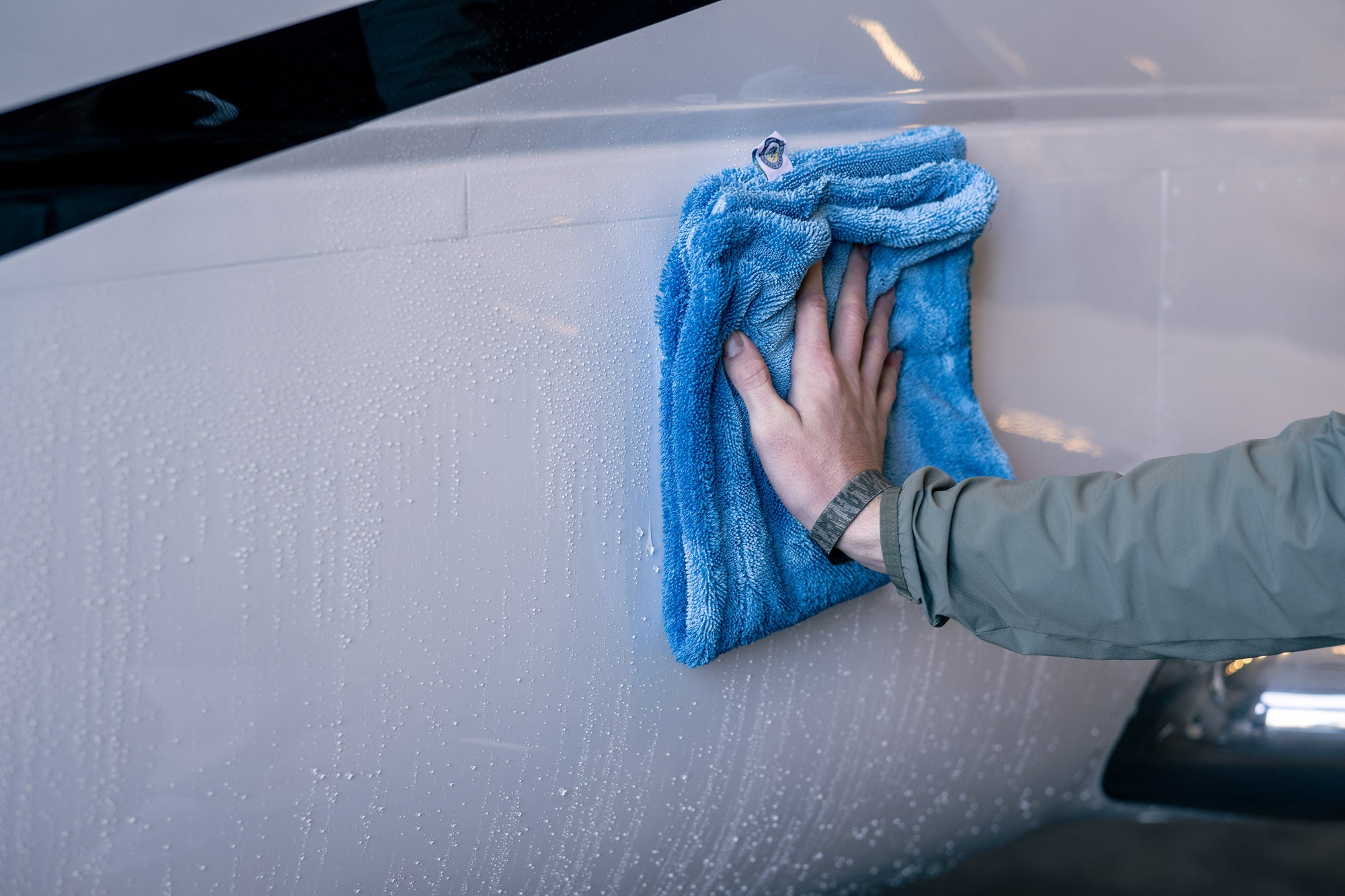 Hand using blue microfiber MagDry towel to dry the surface of a white airplane exterior panel.