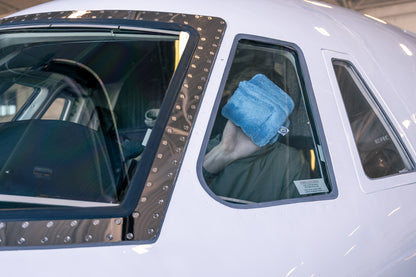 Person using AeroWipe Mini small blue microfiber drying towel on airplane window for precision cleaning