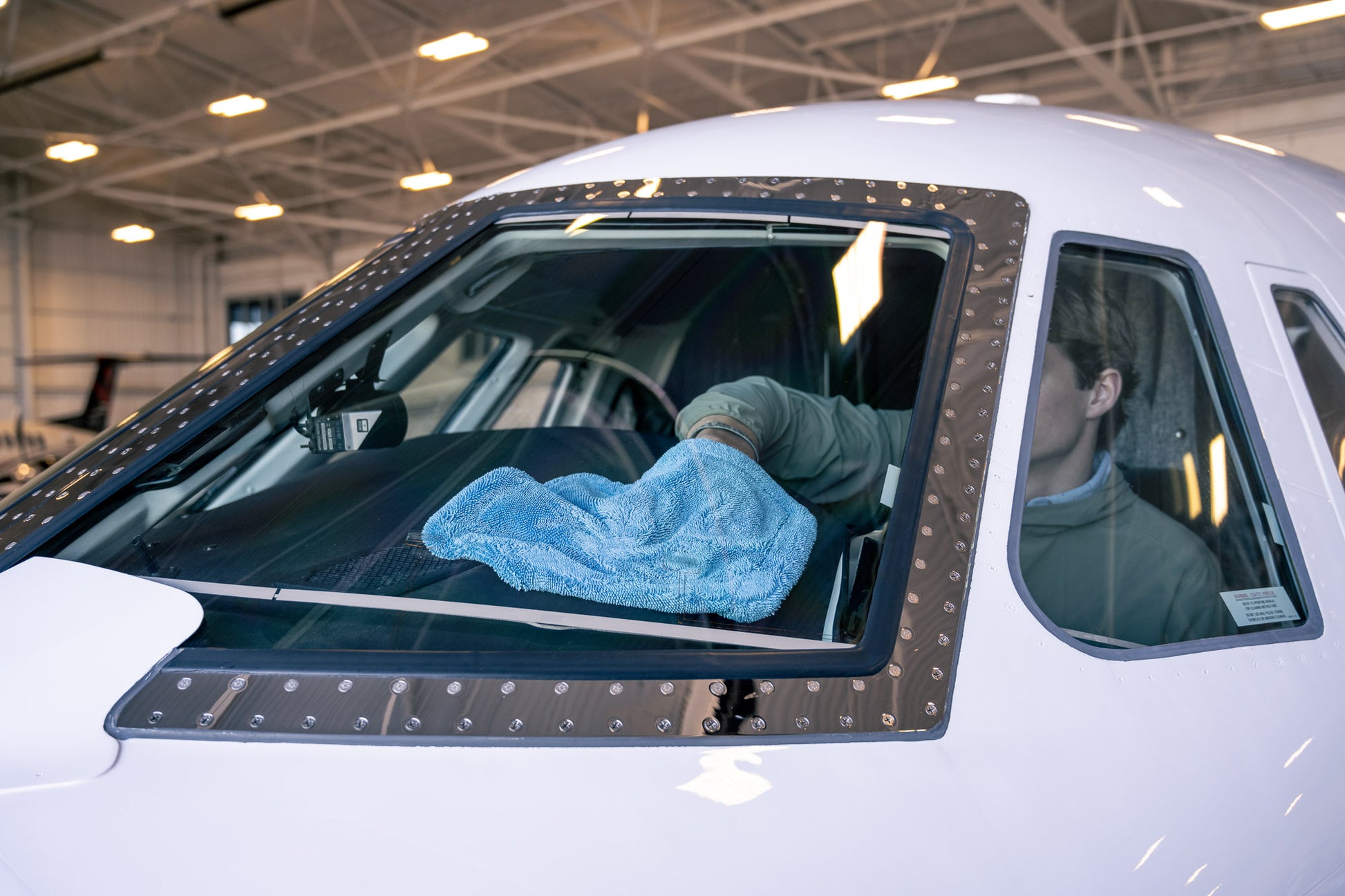 Light blue AeroWipe Mini microfiber towel used to dry the windshield of a white airplane in a hangar environment.
