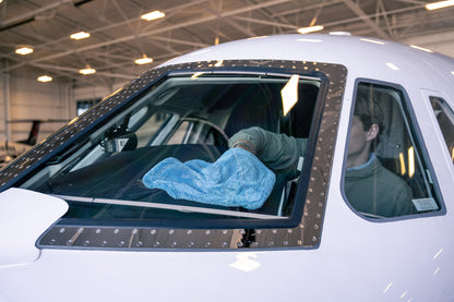 Light blue AeroWipe Mini microfiber towel used to dry the windshield of a white airplane in a hangar environment.