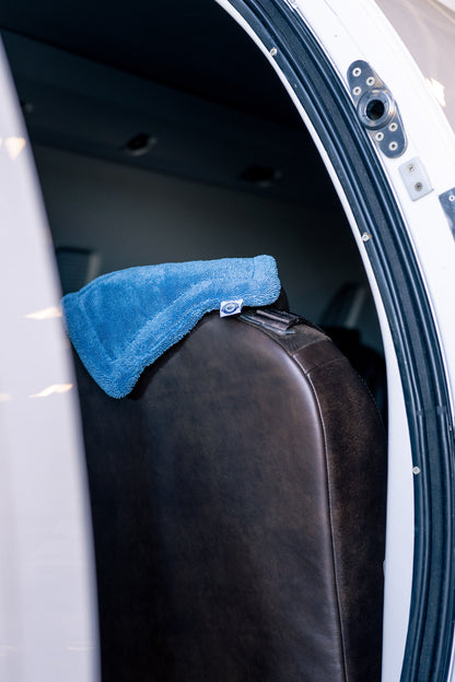 Blue AeroWipe Mini microfiber drying towel resting on a brown leather aircraft seat inside a plane cabin