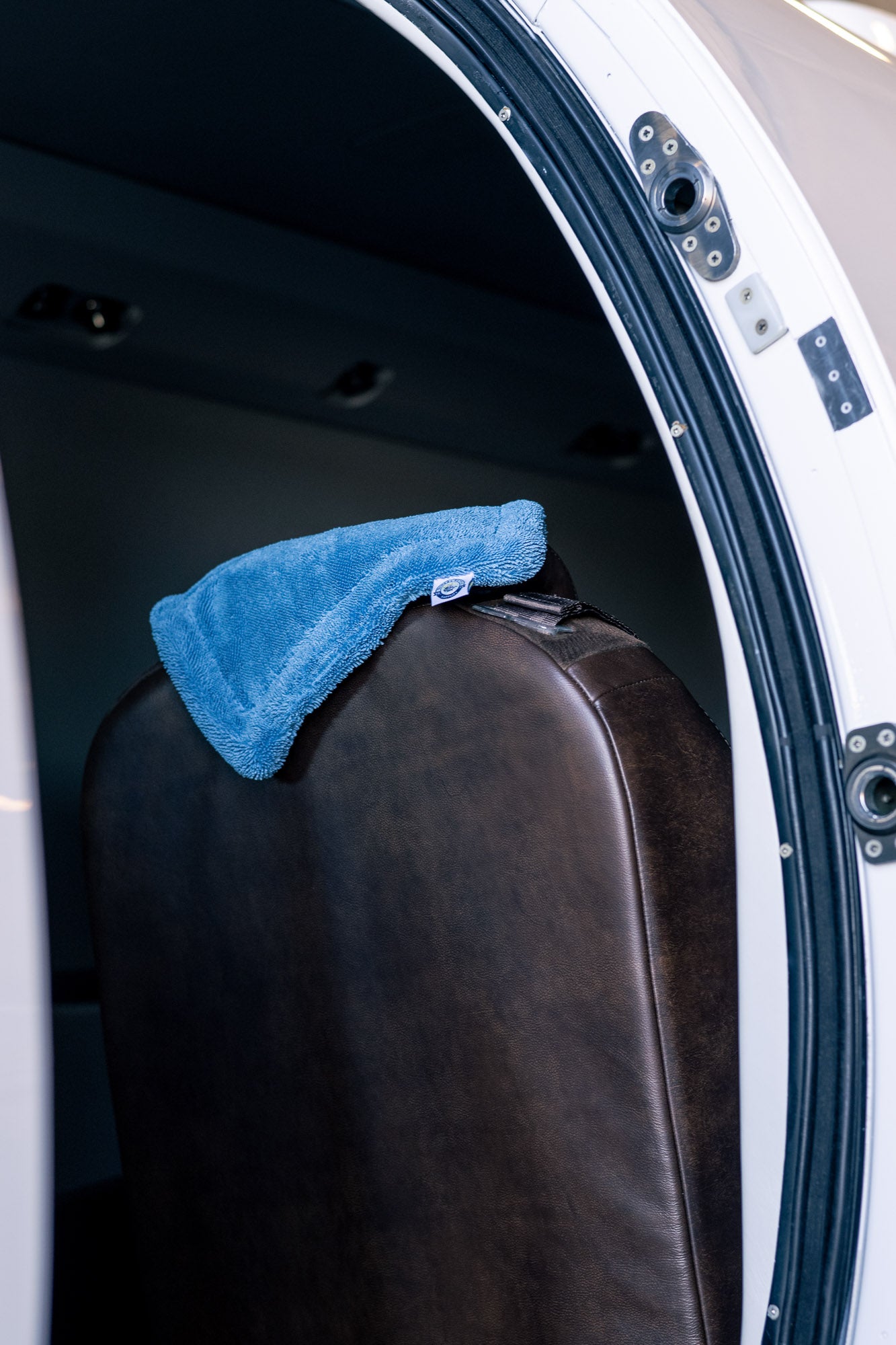 Blue AeroWipe Mini microfiber drying towel draped over a dark brown leather seat inside an aircraft door frame