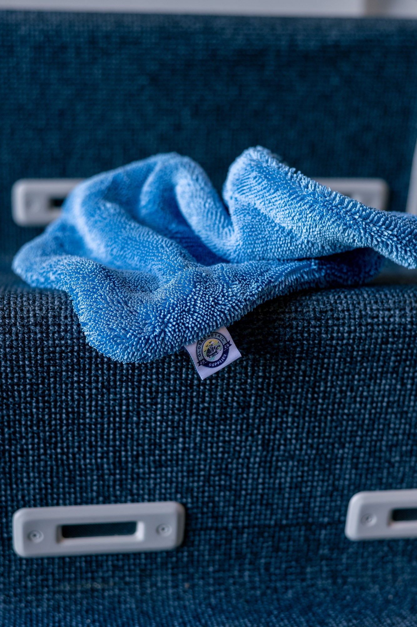 Blue AeroWipe Mini microfiber drying towel draped over blue textured seat in aviation or detailing setting