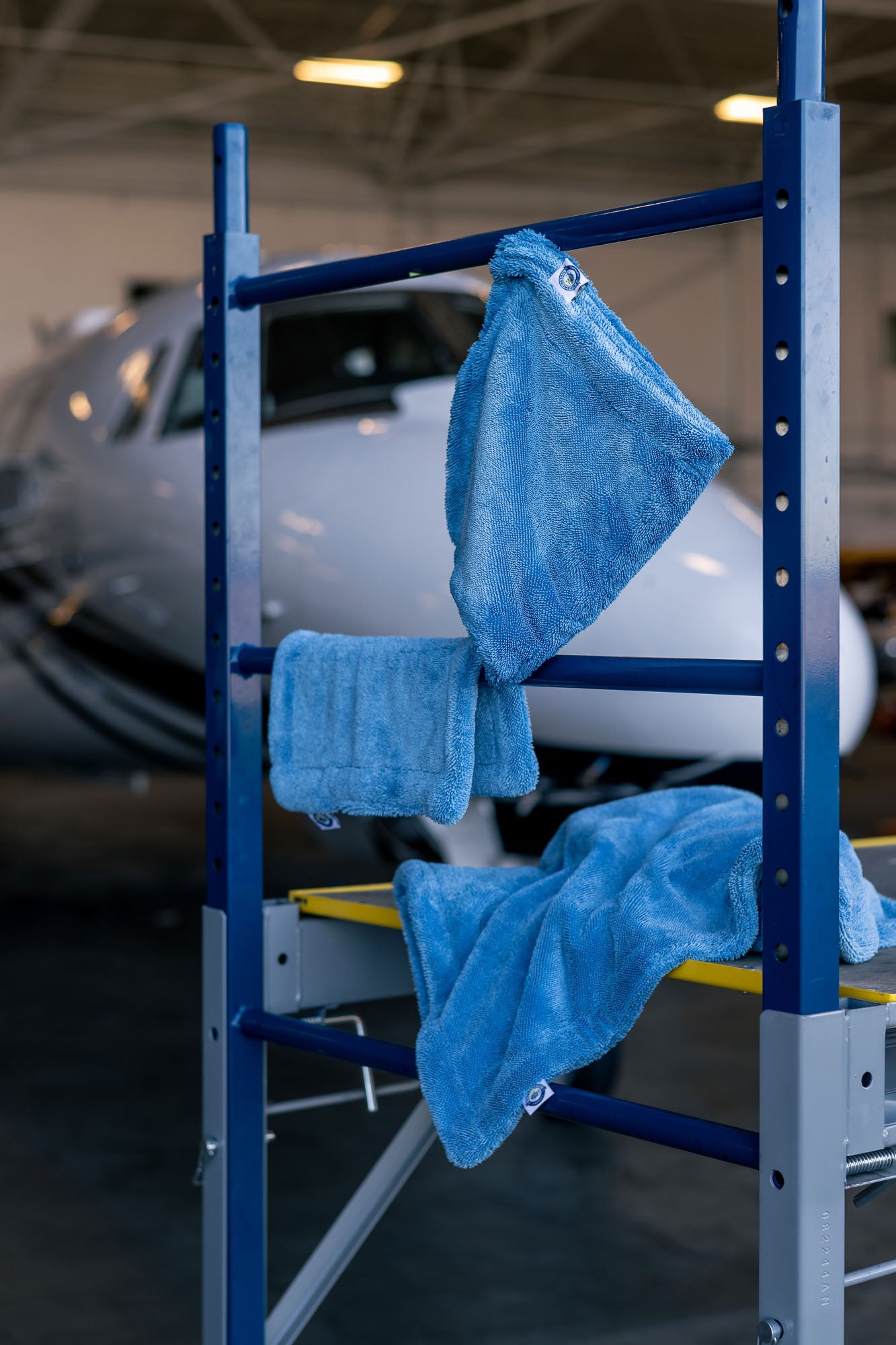 Blue microfiber towels hanging and draped on a blue metal rack inside an aircraft hangar with a plane in the background