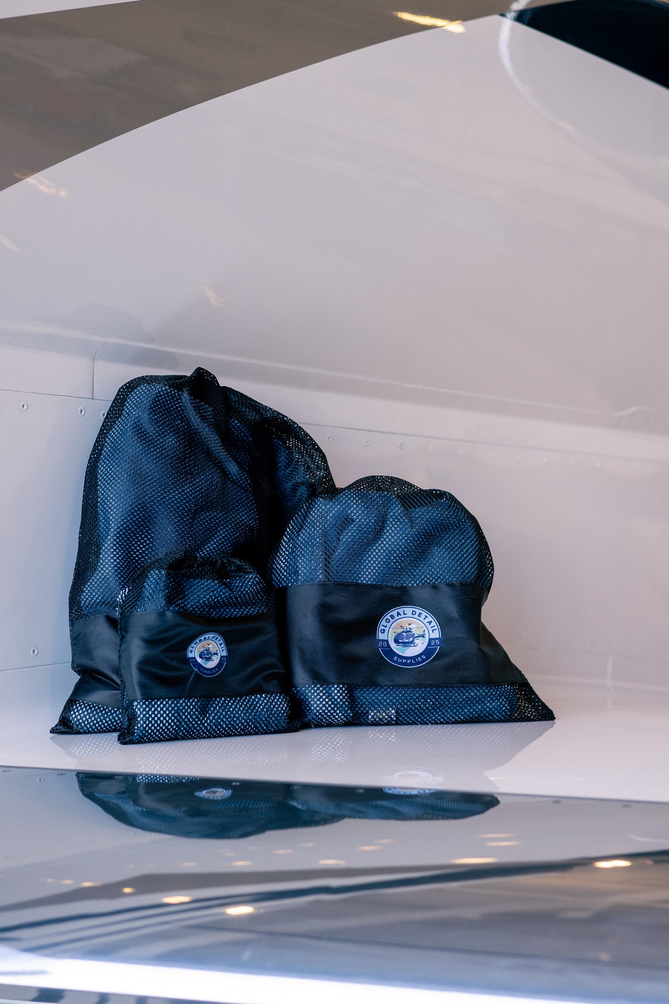 Three black mesh drawstring bags with circular blue and white logo patches placed on a smooth white surface