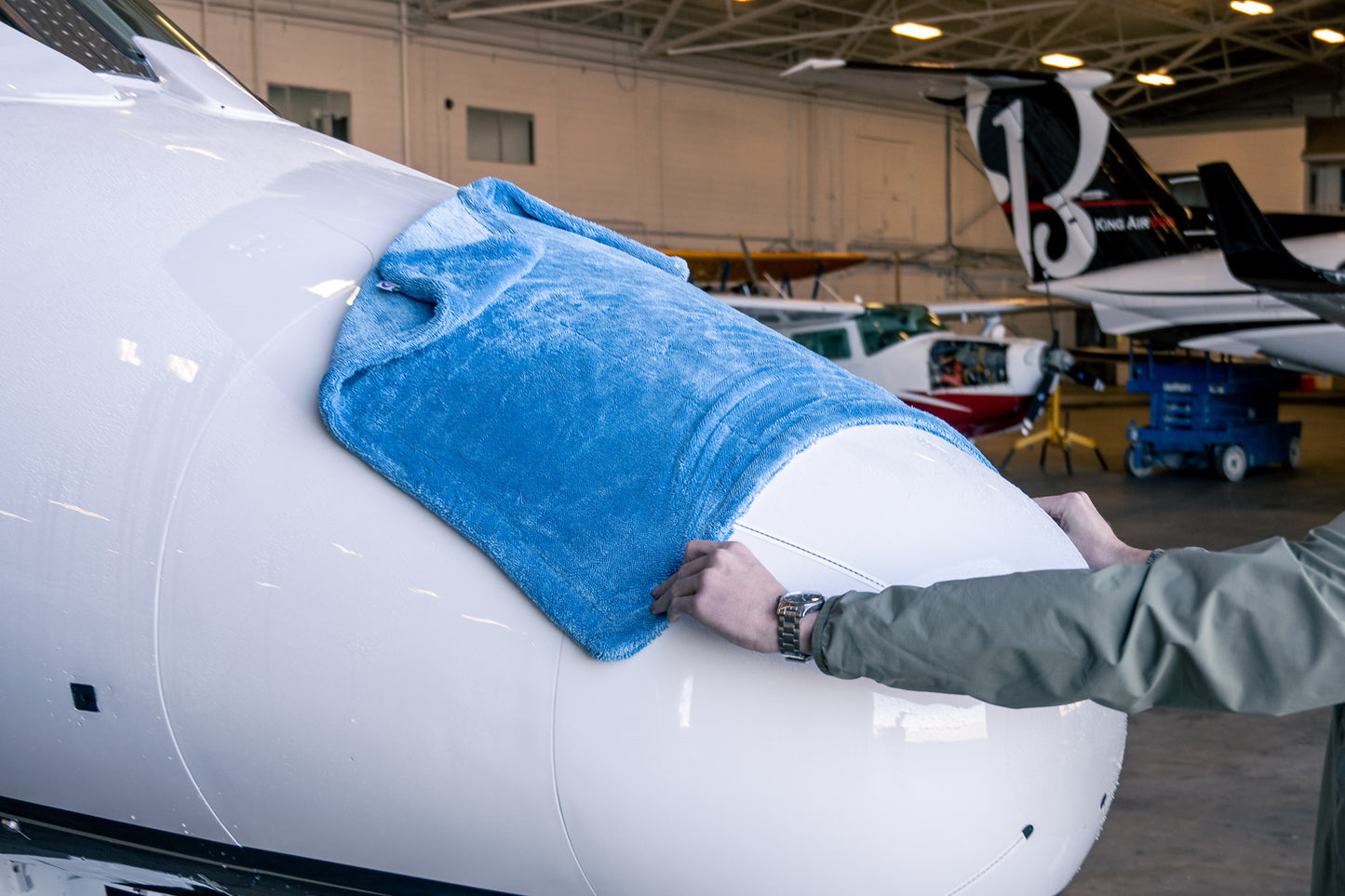 Large blue AeroWipe Max microfiber drying towel covering aircraft nose in a hangar setting with moved hands