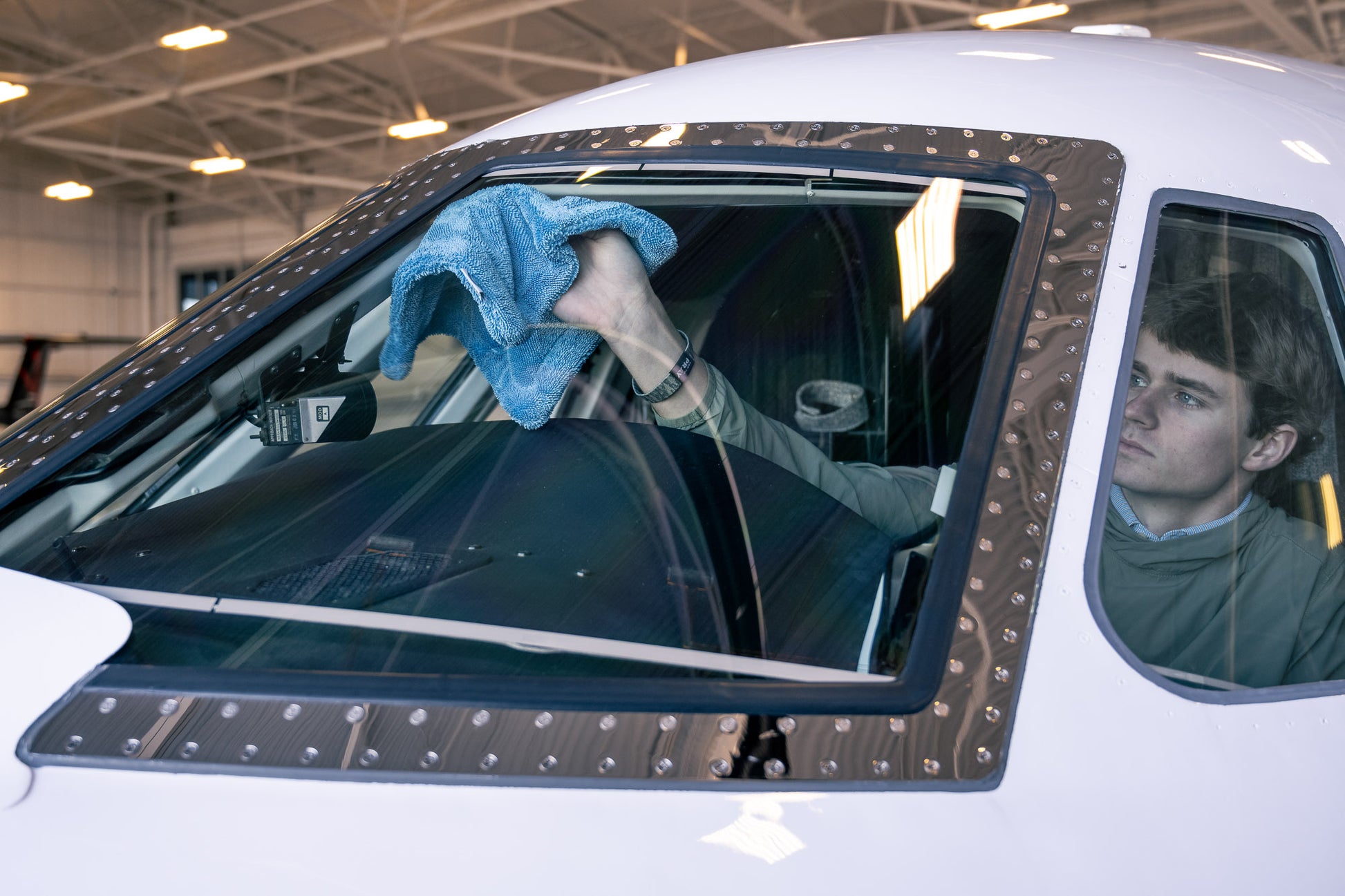 Person using a blue AeroWipe Mini microfiber towel to dry the windshield of a small aircraft inside a hangar