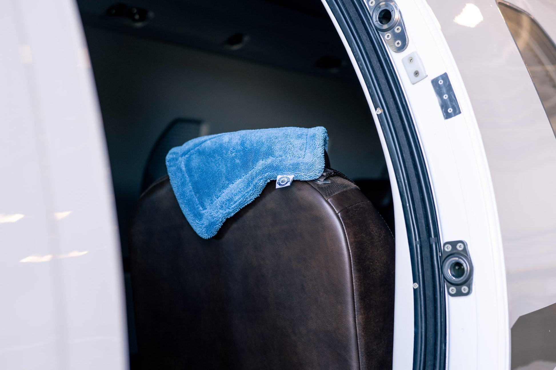 Blue AeroWipe Mini microfiber drying towel draped over a brown leather seat inside a vehicle cabin