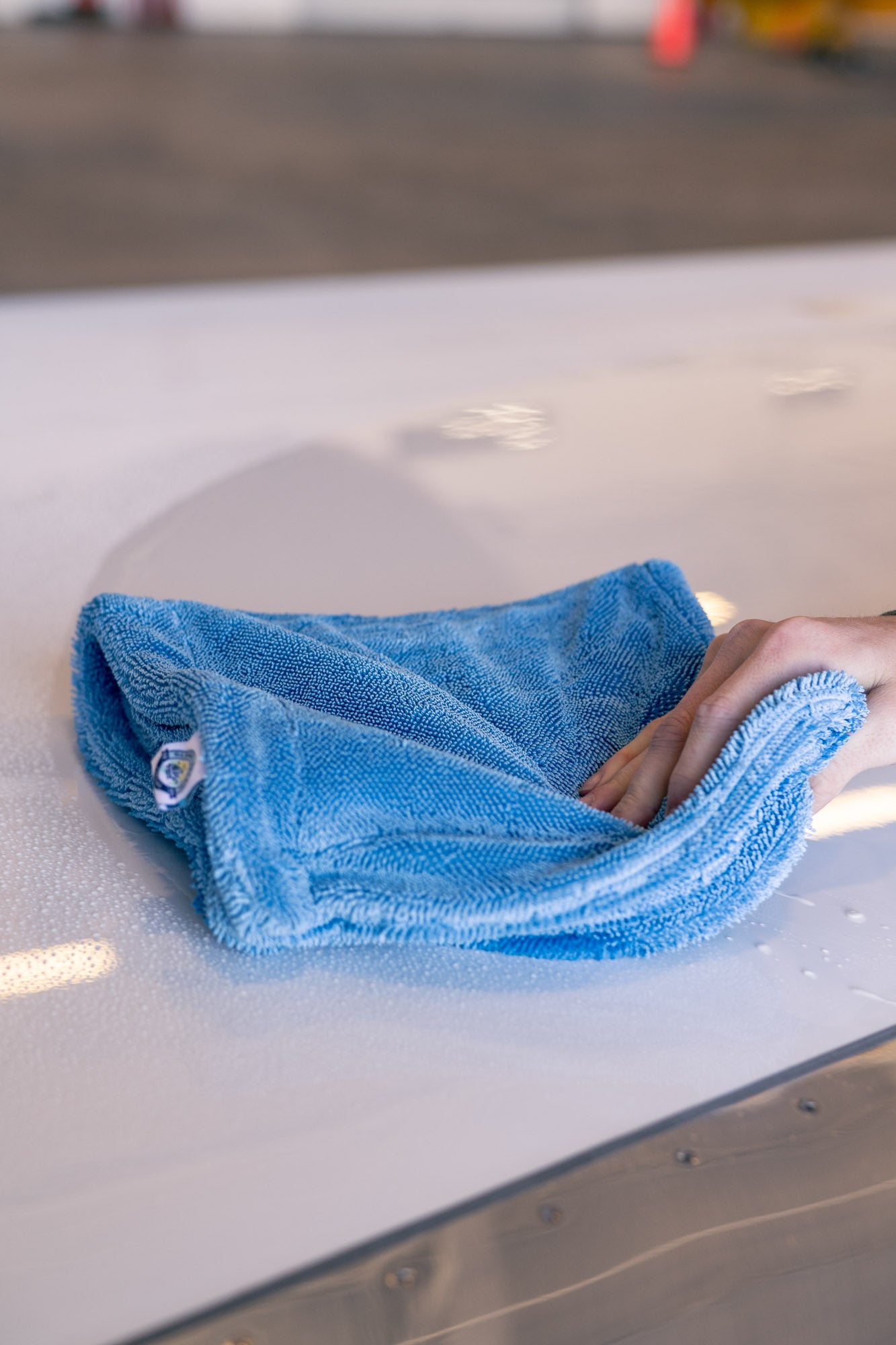 Hand using blue microfiber towel to dry a wet white surface, demonstrating MagDry magnet-embedded drying towel usage