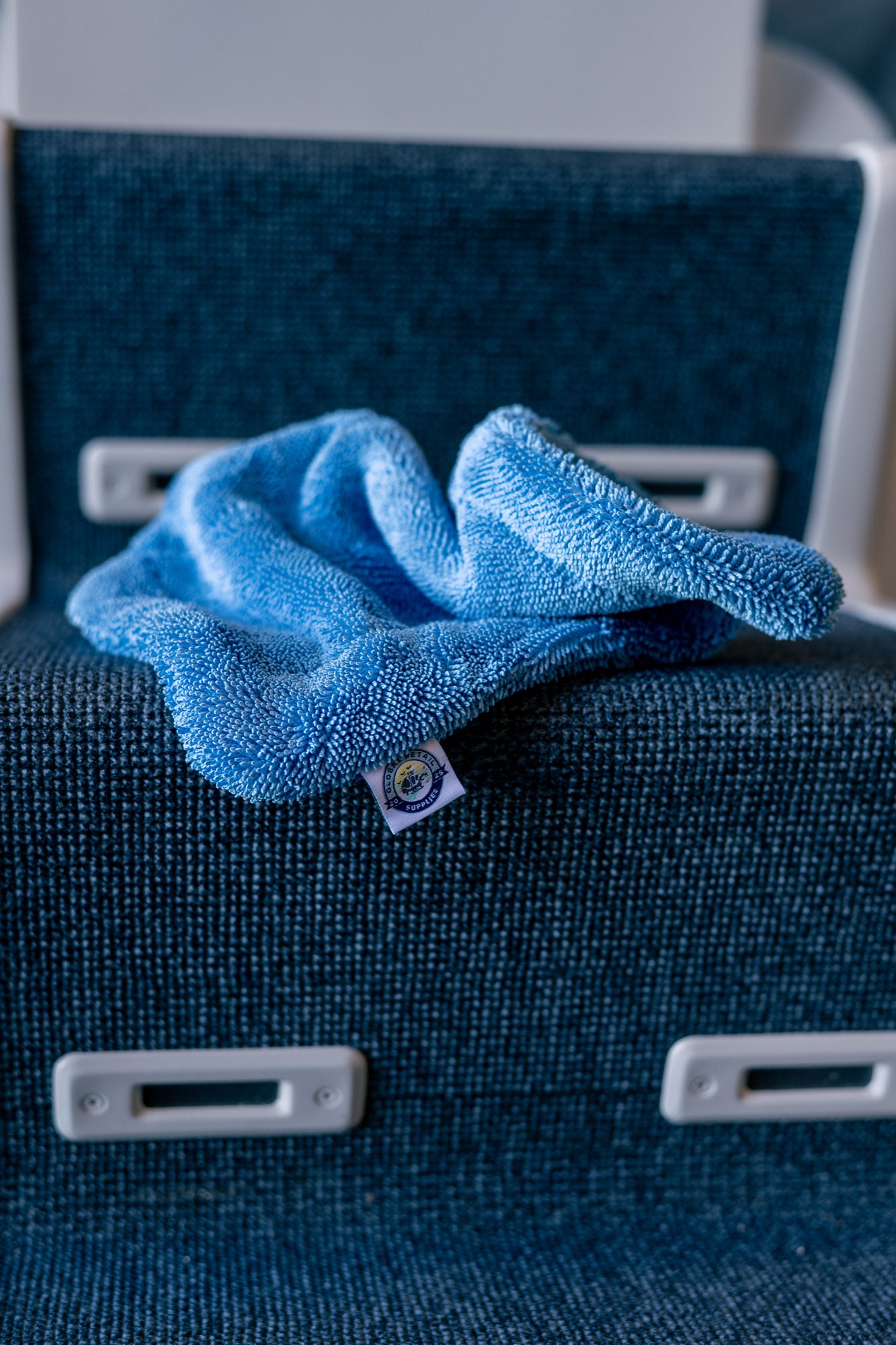 Blue AeroWipe Mini microfiber drying towel laid on textured dark blue seating surface with white plastic fixtures