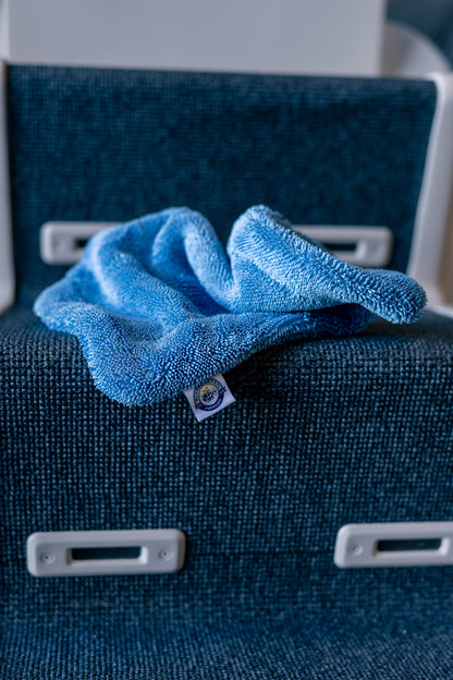 Blue AeroWipe Mini microfiber drying towel laid on textured dark blue seating surface with white plastic fixtures