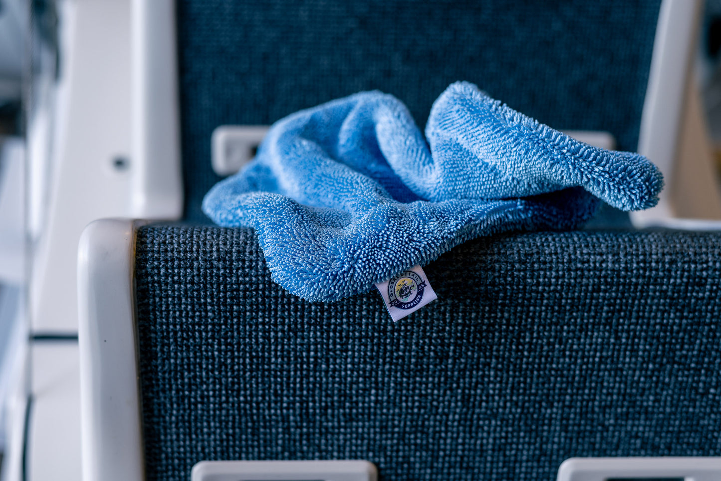 Blue AeroWipe Mini microfiber drying towel draped over a textured gray-blue airplane seat armrest